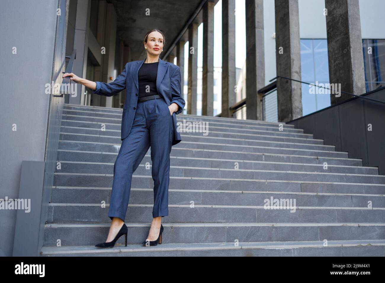 Donna vestita con stile che si posa sulle scale di un edificio moderno Foto Stock