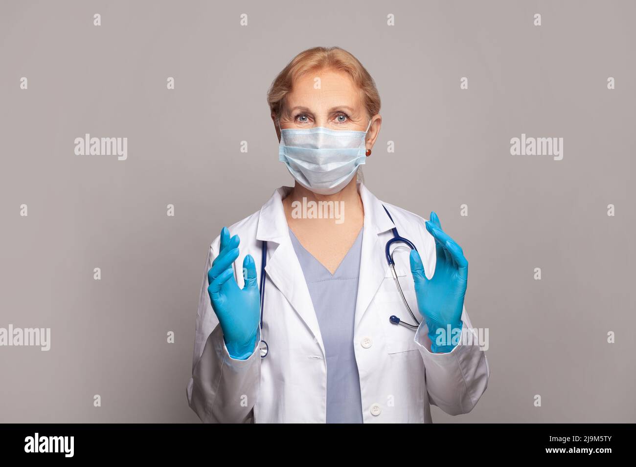 Medico femminile in piedi e mostrando il gesto su sfondo grigio Foto Stock