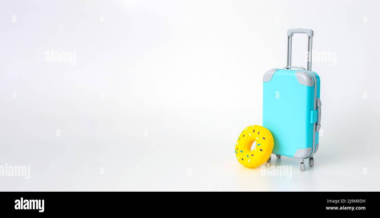 Una valigia blu su ruote e un supporto giallo gonfiabile ciambella su un fondo bianco largo. Foto Stock