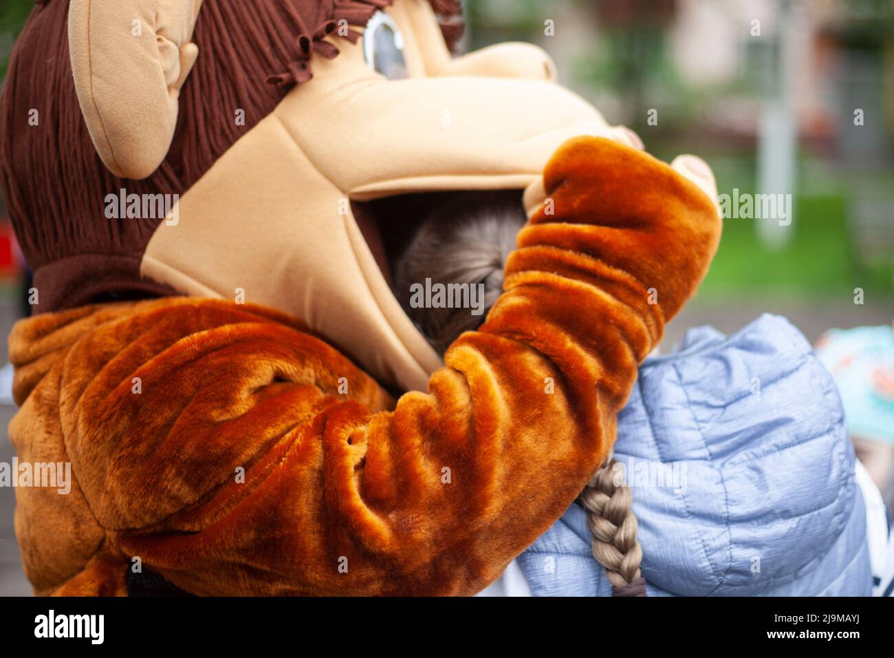 Il bambino gioca con la bambola di crescita. Animatore al festival intrattiene i bambini. La ragazza tiene l'uomo in costume da scimmia. Riposarsi nel parco. Dettagli della scena. Foto Stock