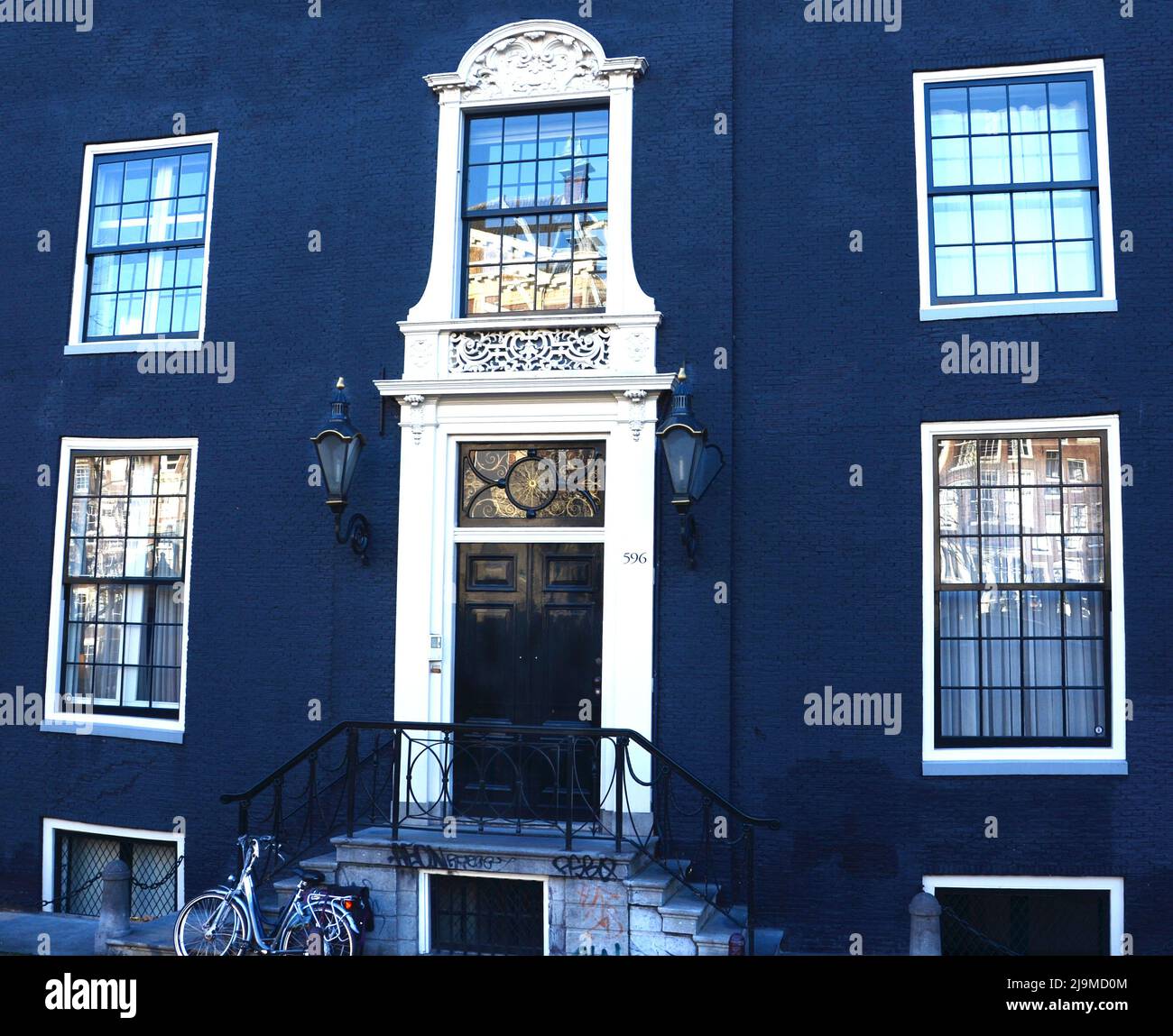 Facciata di una tipica casa olandese con pareti in mattoni dipinti blu, gradini, porta d'ingresso, finestre di vetro e biciclette nella popolare strada del quartiere, Paesi Bassi Foto Stock