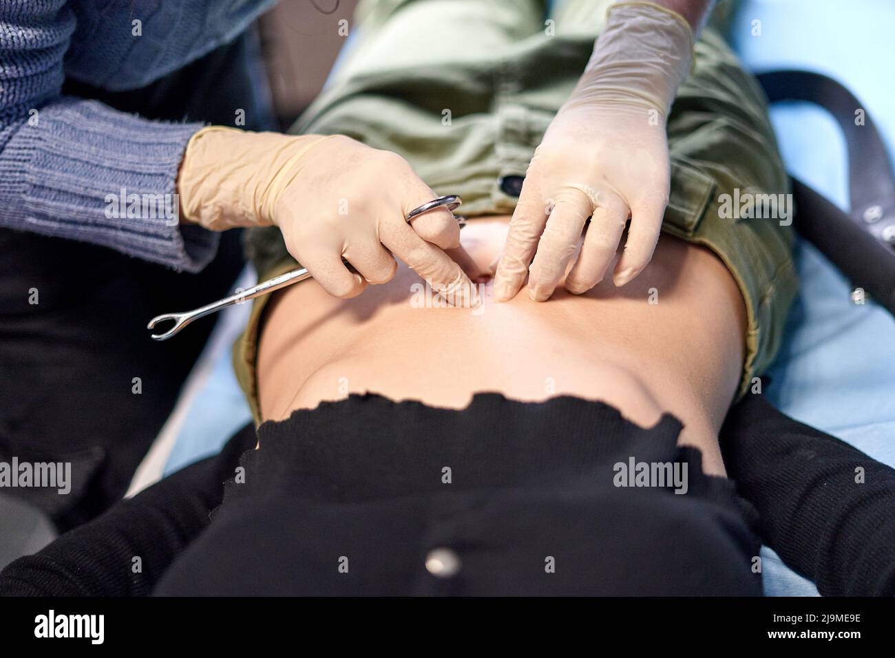 Alto angolo di anonima modifica del corpo artista pizzicando il pulsante della pancia del cliente femminile durante la procedura di piercing in salone Foto Stock