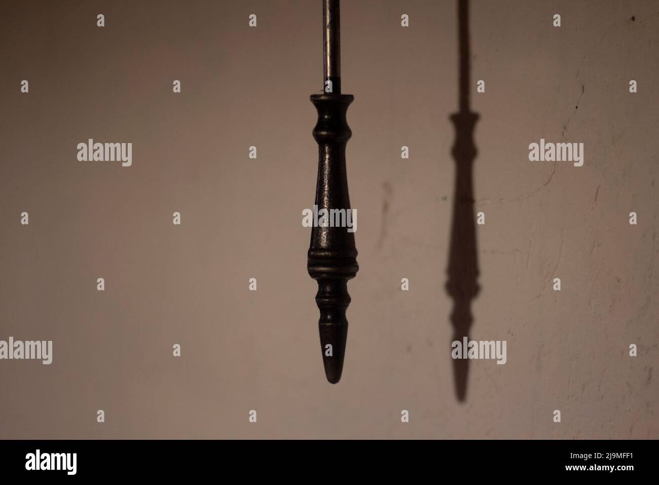 L'oggetto in ferro proietta l'ombra sul muro. Figura di pendolo di vecchio orologio. Cosa in camera. Foto Stock