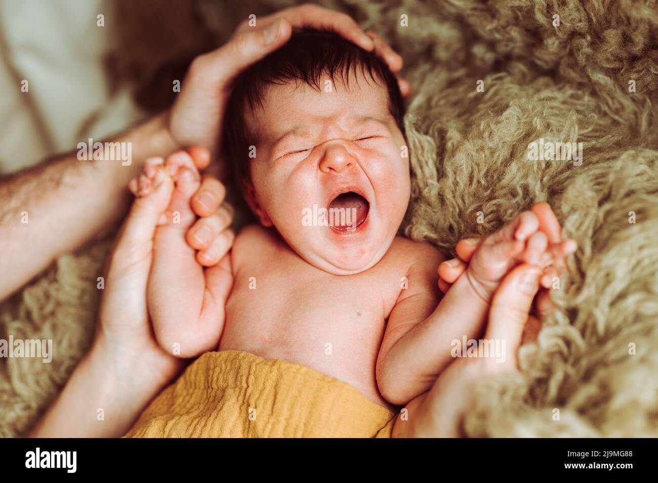 Alto angolo di giovane madre e padre irriconoscibile con capelli scuri che tengono la mano di adorabile neonato yawning sdraiato e dormire su letto morbido in da Foto Stock
