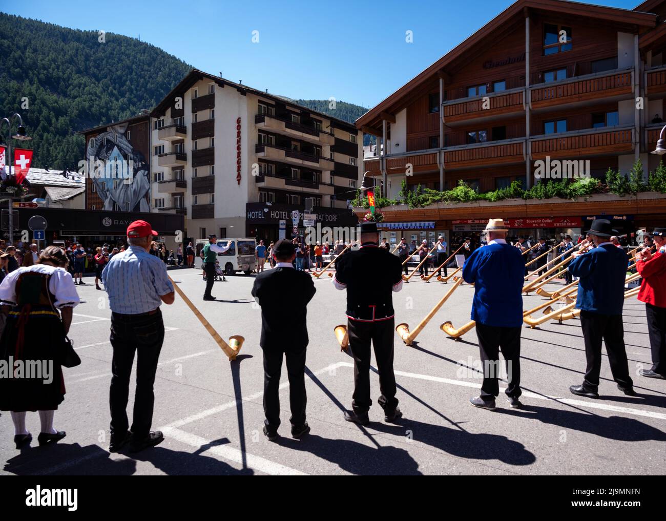 I musicisti svizzeri suonano l'alphorn, uno strumento musicale tradizionale guidato da un direttore del coro sulla strada principale del villaggio di Zermatt. Foto Stock