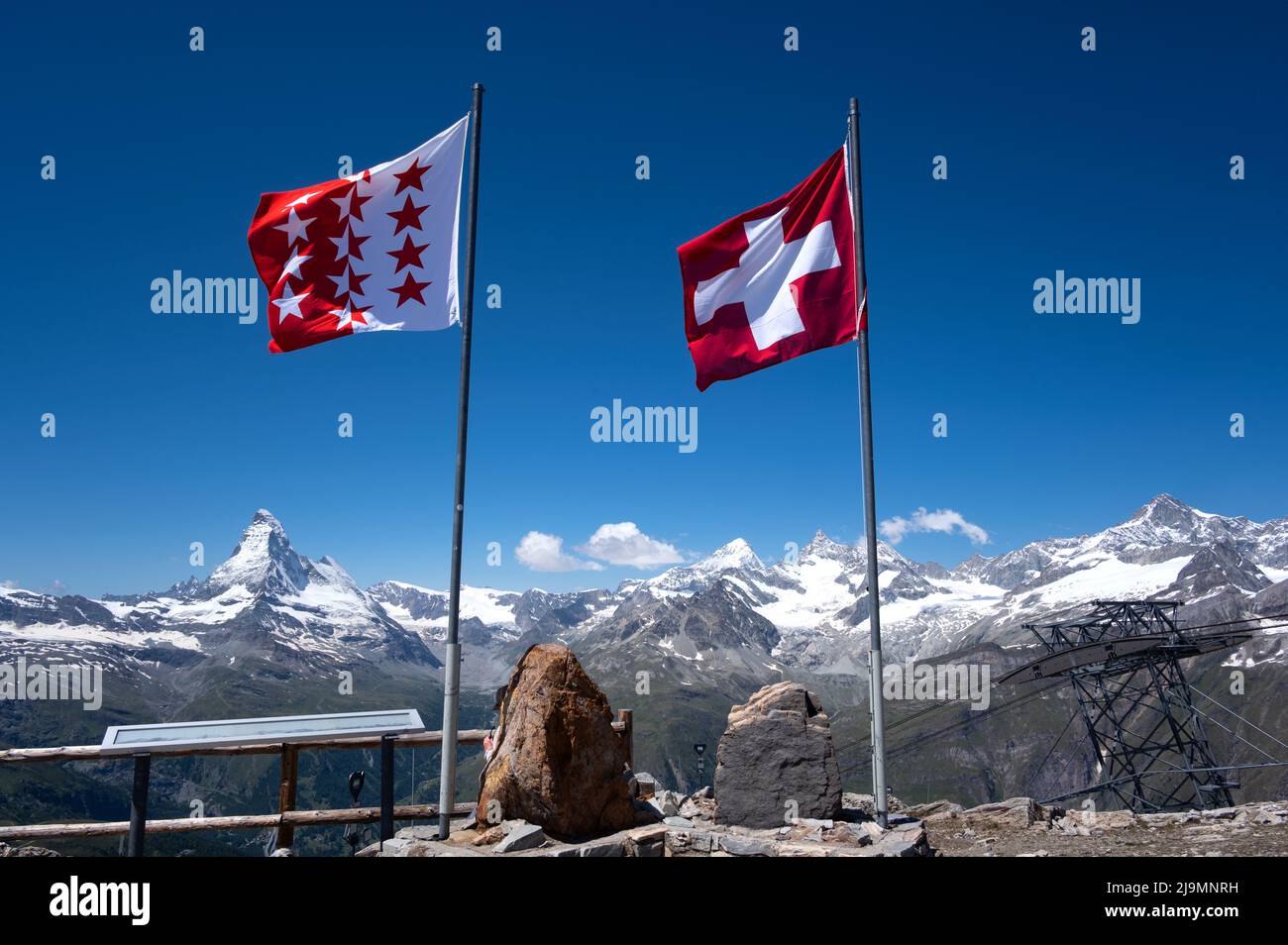 Vista della bandiera svizzera in cima alla cima del Rothorn con la splendida cima del ghiacciaio del Cervino sullo sfondo. Popolare Sunrise Spot a Zermatt Foto Stock