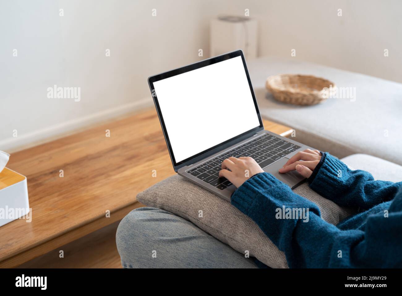 Vista dall'alto immagine mockup di una donna che lavora e digita su un computer portatile con schermo vuoto mentre si siede su un divano a casa Foto Stock