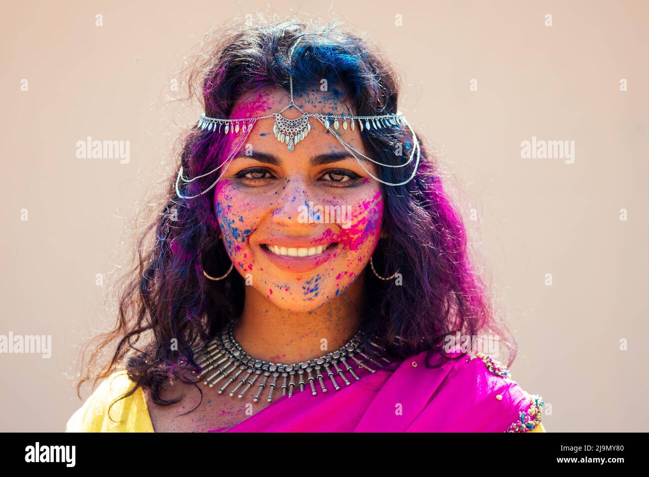 Donna indiana modello neve-bianco sorriso sul colore holi festival.indiano Donna in tradizionale sari abito con capelli ricci nero in una vernice rosa e blu e. Foto Stock