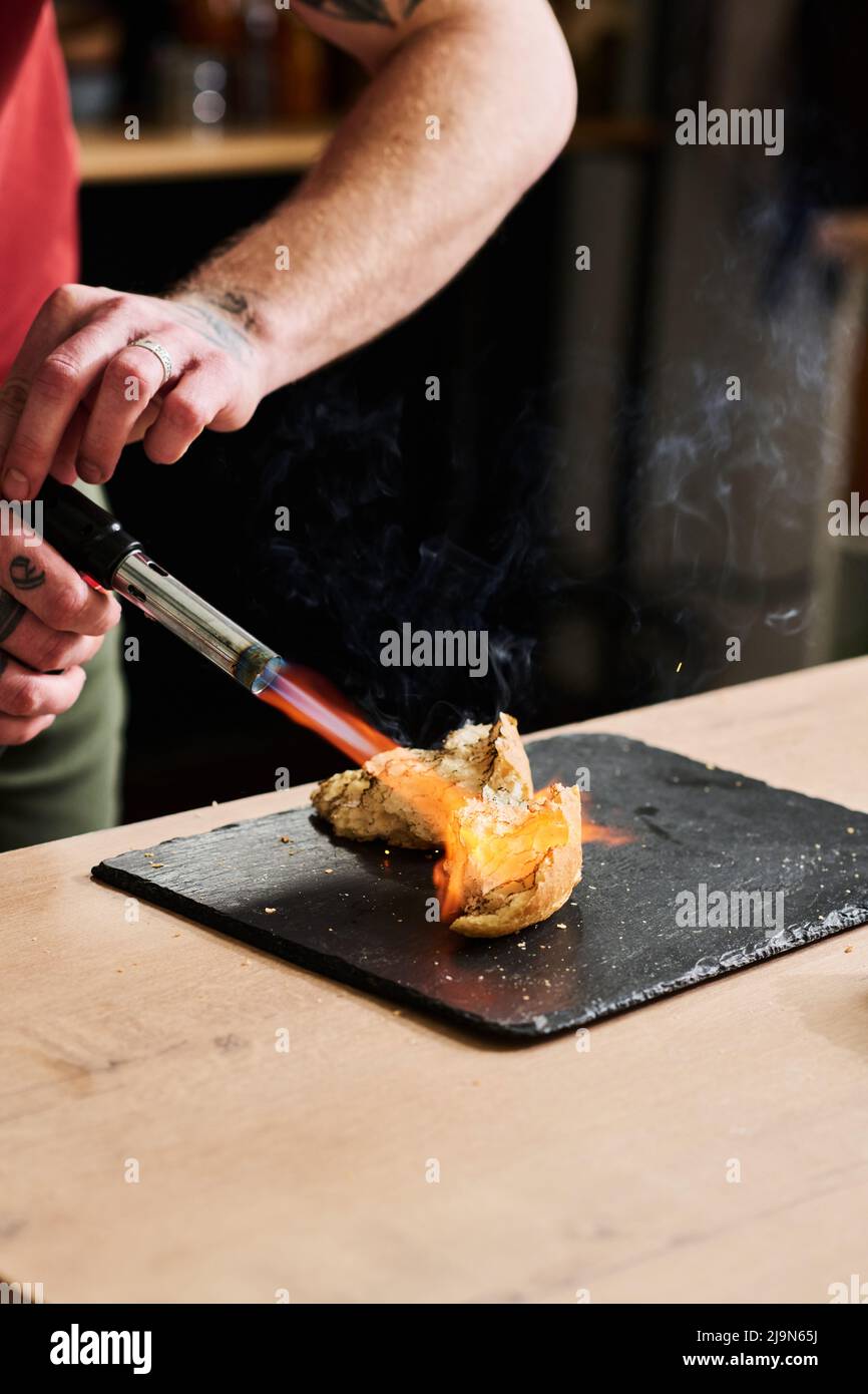 Uomo irriconoscibile preparare il pasto in cucina loft a casa tostando il pane con fiamma torcia Foto Stock