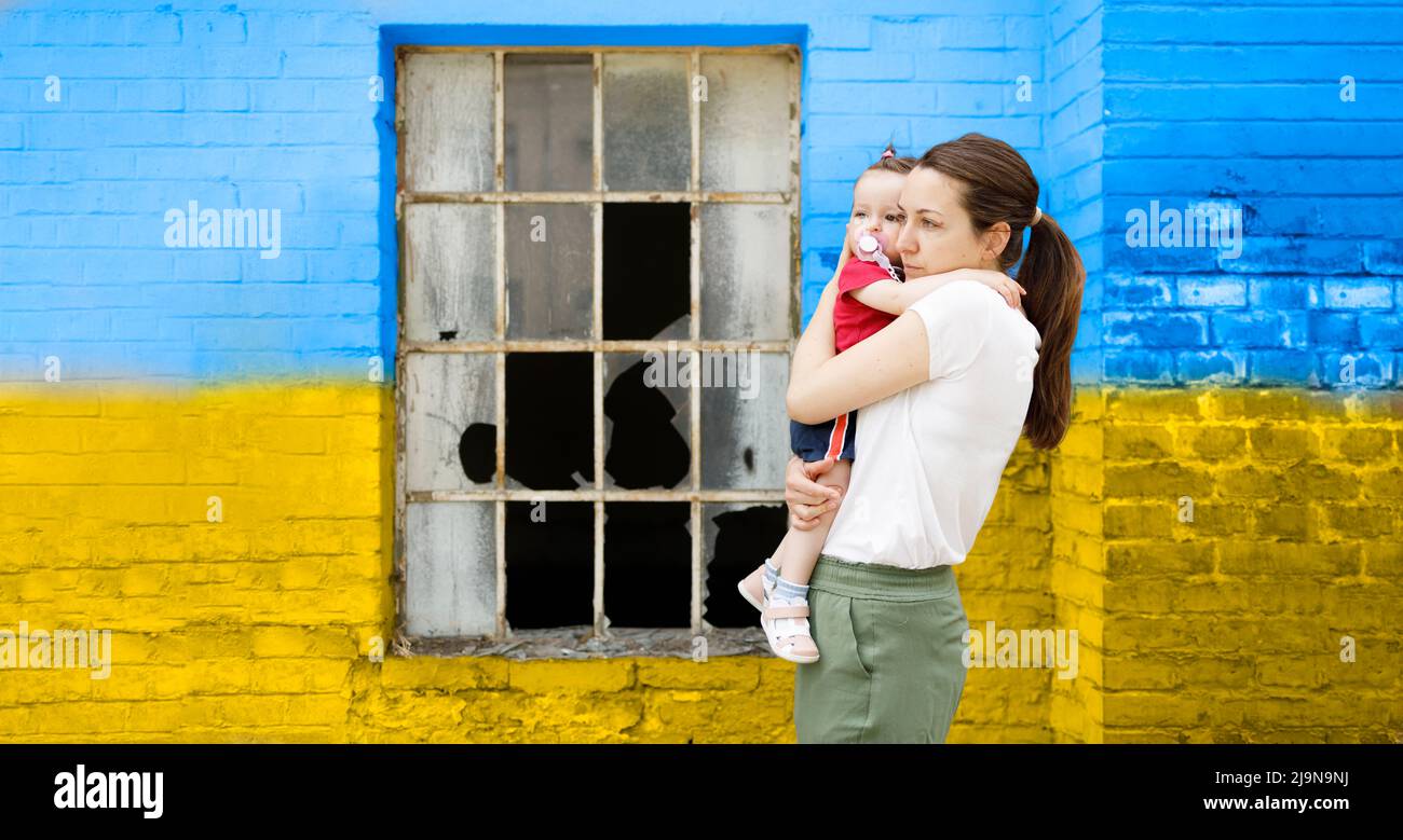 Madre preoccupata che tiene il suo bambino davanti ad una finestra distrutta Foto Stock