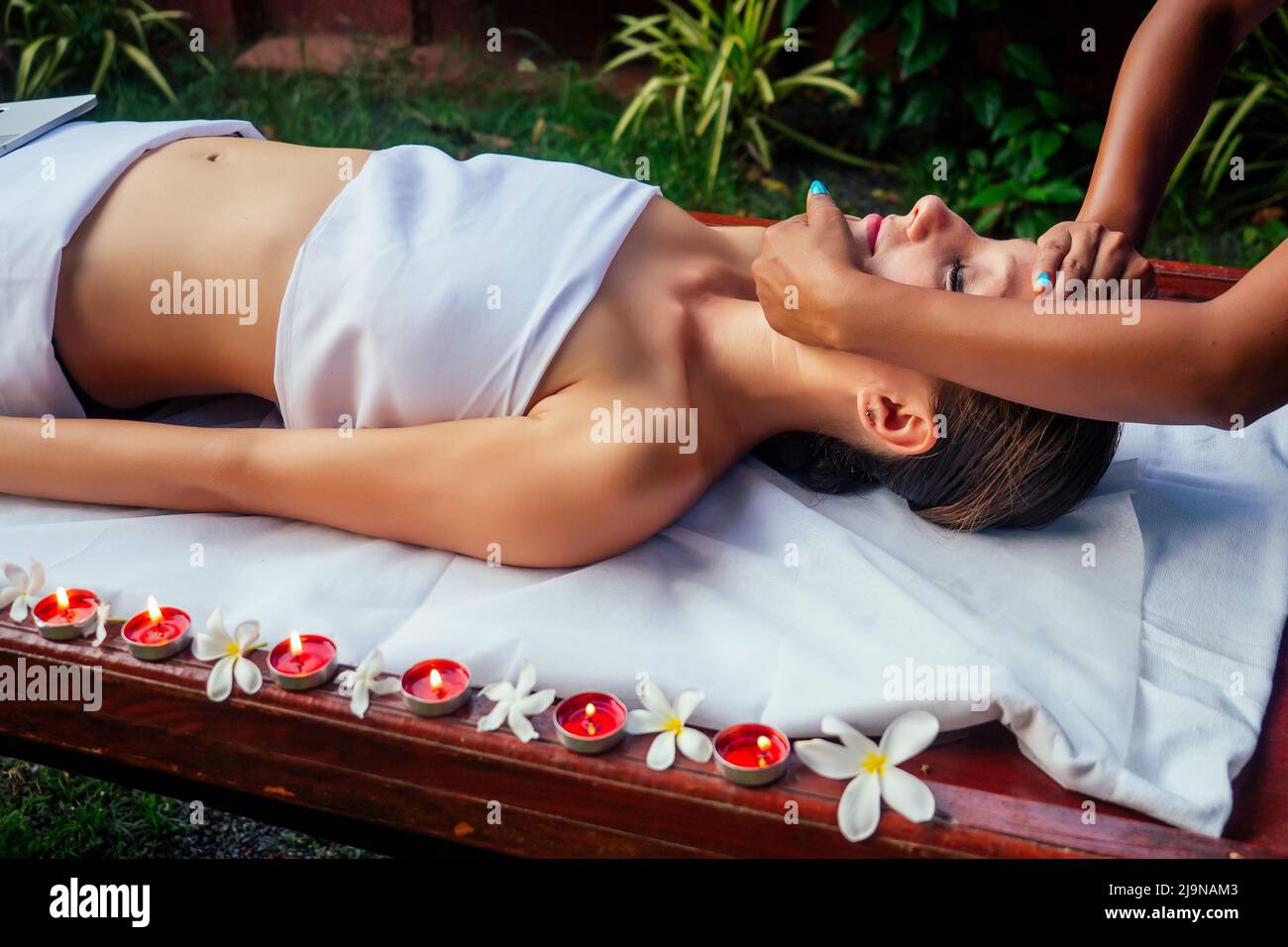 Donna che ha ayurveda spa trattamento in asia salone testa, capelli e viso massaggio sirodhara candele e fiori sullo sfondo Foto Stock