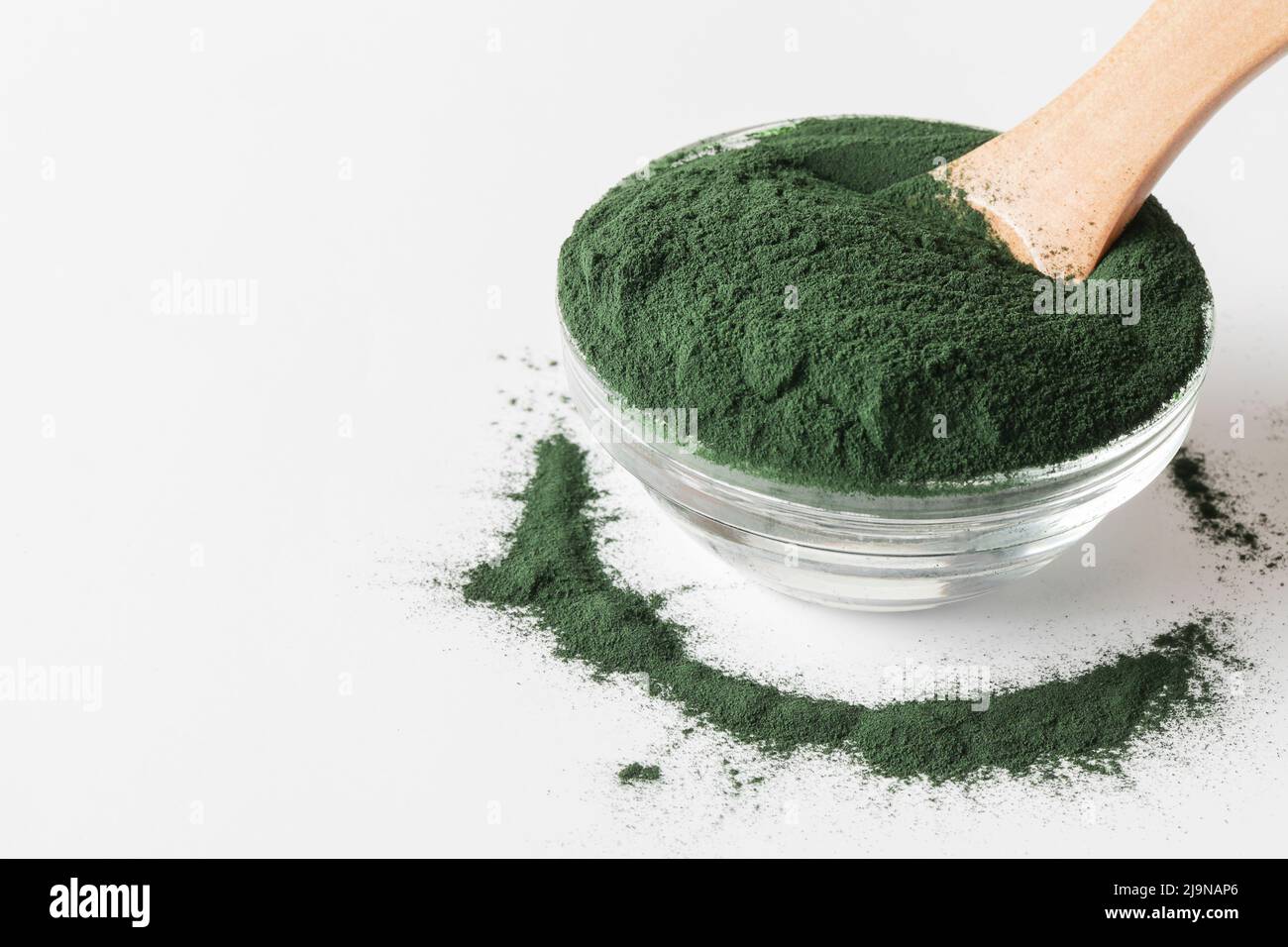 additivi naturali e superfood. polvere di alghe spirulina verde in vetro con cucchiaio di legno su sfondo bianco. stile di vita sano. alimenti biologici Foto Stock