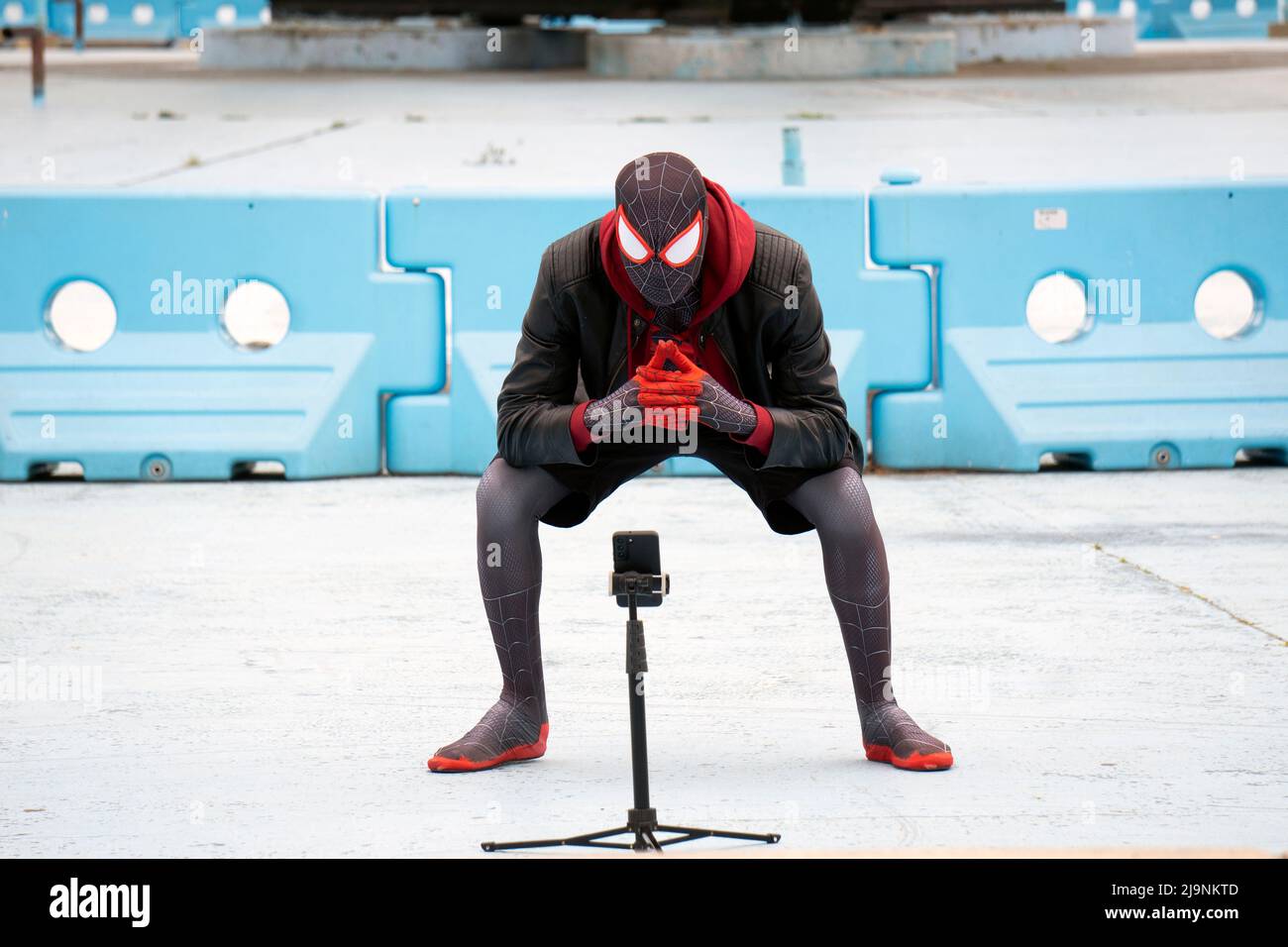 Con l'aiuto di un treppiede, Spiderman prende alcuni selfie sotto l'Unisphere in Flushing Meadows Corona Park in regine, New York City. Foto Stock