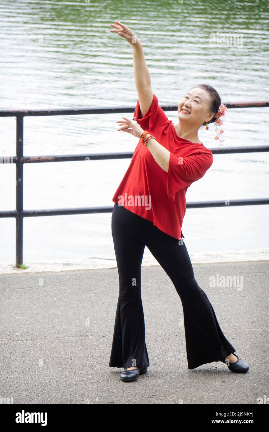 Una graziosa donna asiatica americana che ama ballare pone per le foto vicino ad un lago in un parco a Queens, New York City. Foto Stock