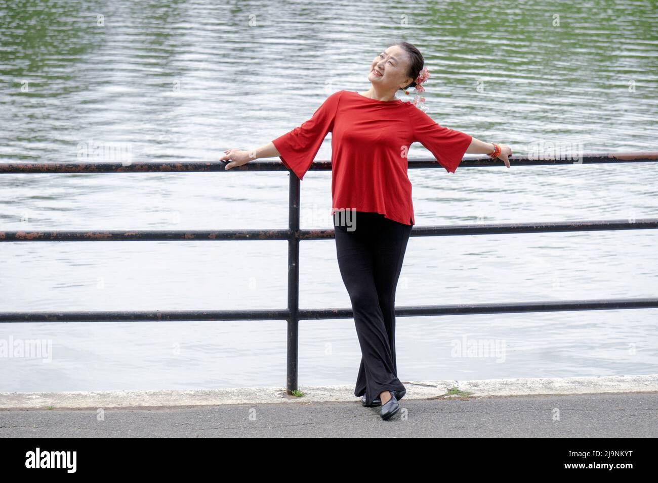Una graziosa donna asiatica americana che ama ballare pone per le foto vicino ad un lago in un parco a Queens, New York City. Foto Stock