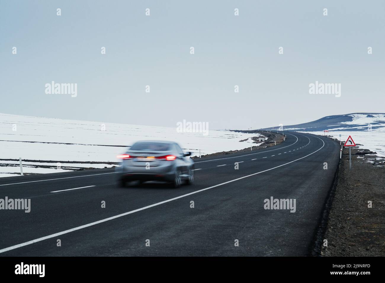 Vista diagonale di una strada asfaltata e in curva con un movimento sfocato auto, corsie e neve in inverno. Foto Stock