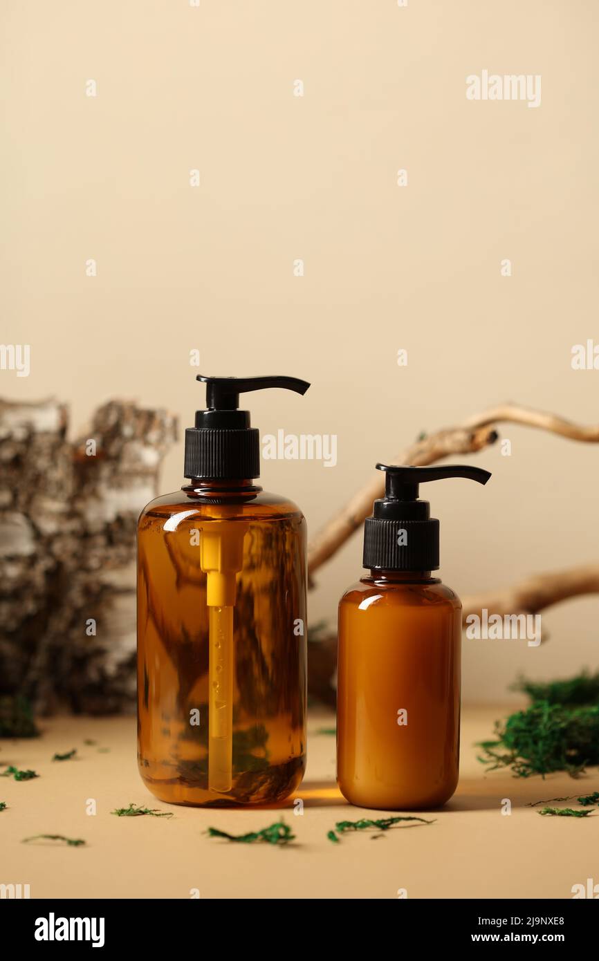 Dispenser in vetro ambrato con shampoo naturale e gel doccia. Ramo di albero, betulla corteccia, muschio su sfondo. Foto Stock