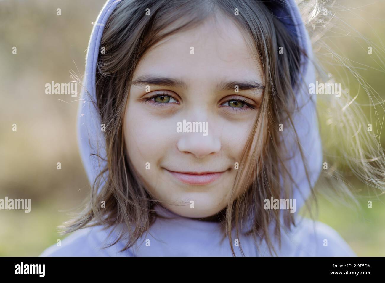 Un ritratto di bella felpa con cappuccio girlin bambino in piedi nel parco estivo guardando la macchina fotografica sorridendo felicemente. Foto Stock