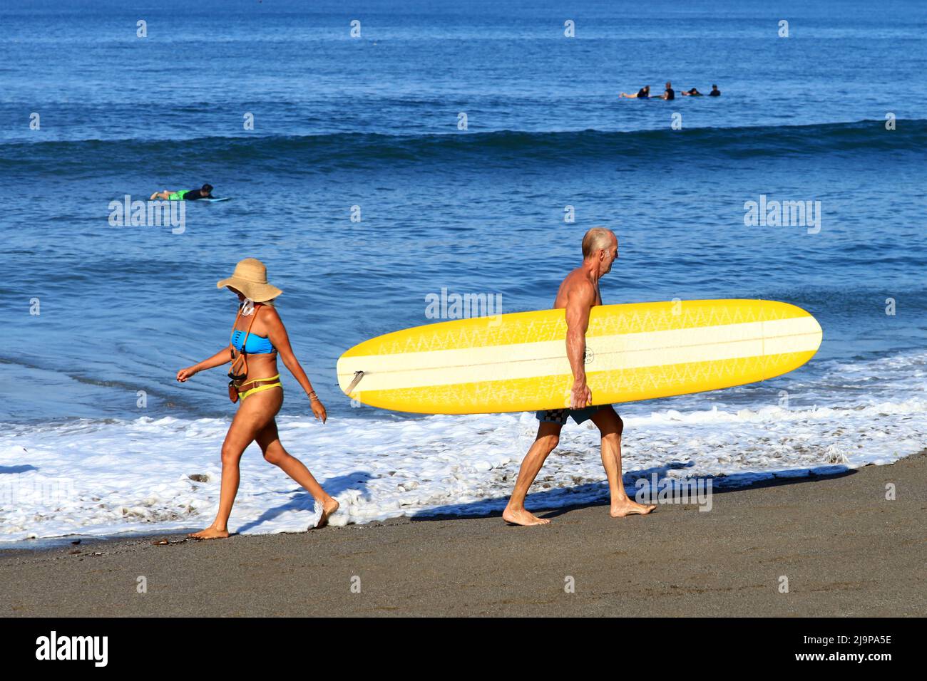 Persone che camminano sulla sabbia trasportando tavole da surf a Batu Bolong Beach, Canggu, Bali, Indonesia Foto Stock