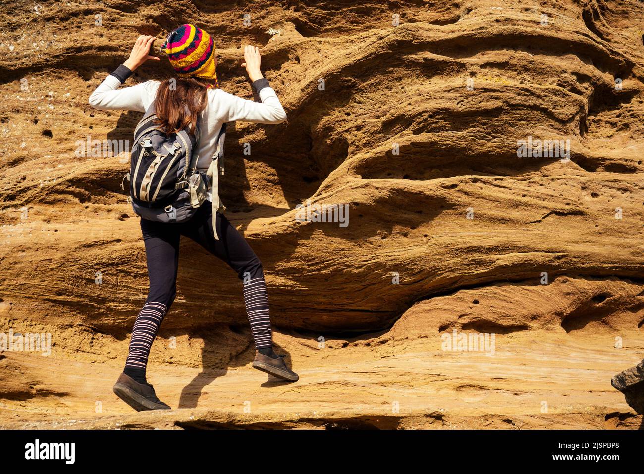 Bella donna turistica giovane, sottile e sportiva, in un simpatico cappello da Nepal lana yak arrampicata grande roccia arrampicate su massi canyon pietre Foto Stock