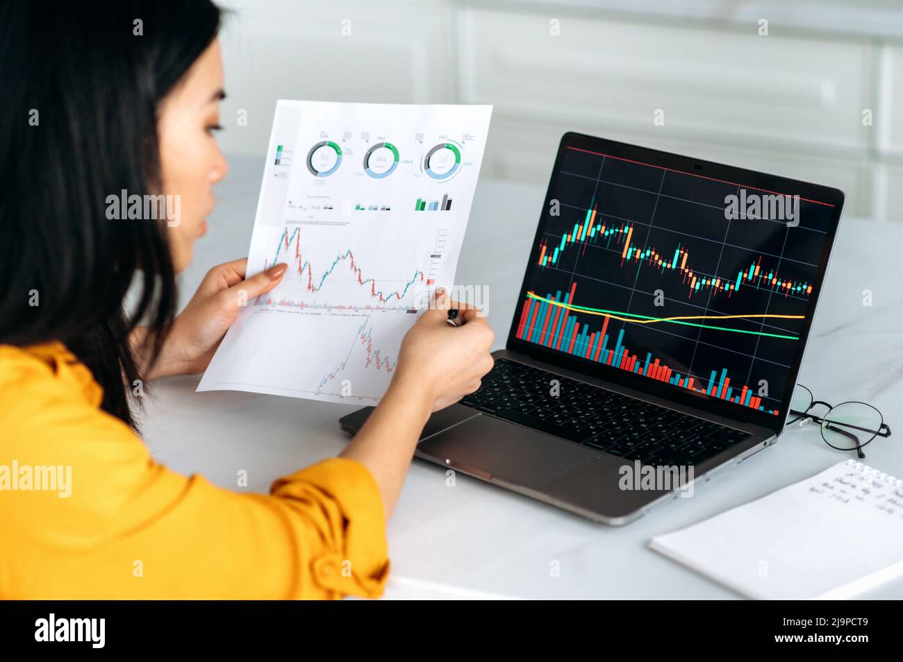 Una donna intelligente di successo Crypto trader, un investitore, utilizza il laptop, analizza le tabelle di trading nel mercato azionario dello scambio di criptovaluta digitale, analizza, acquista e vende le monete criptovalute Foto Stock