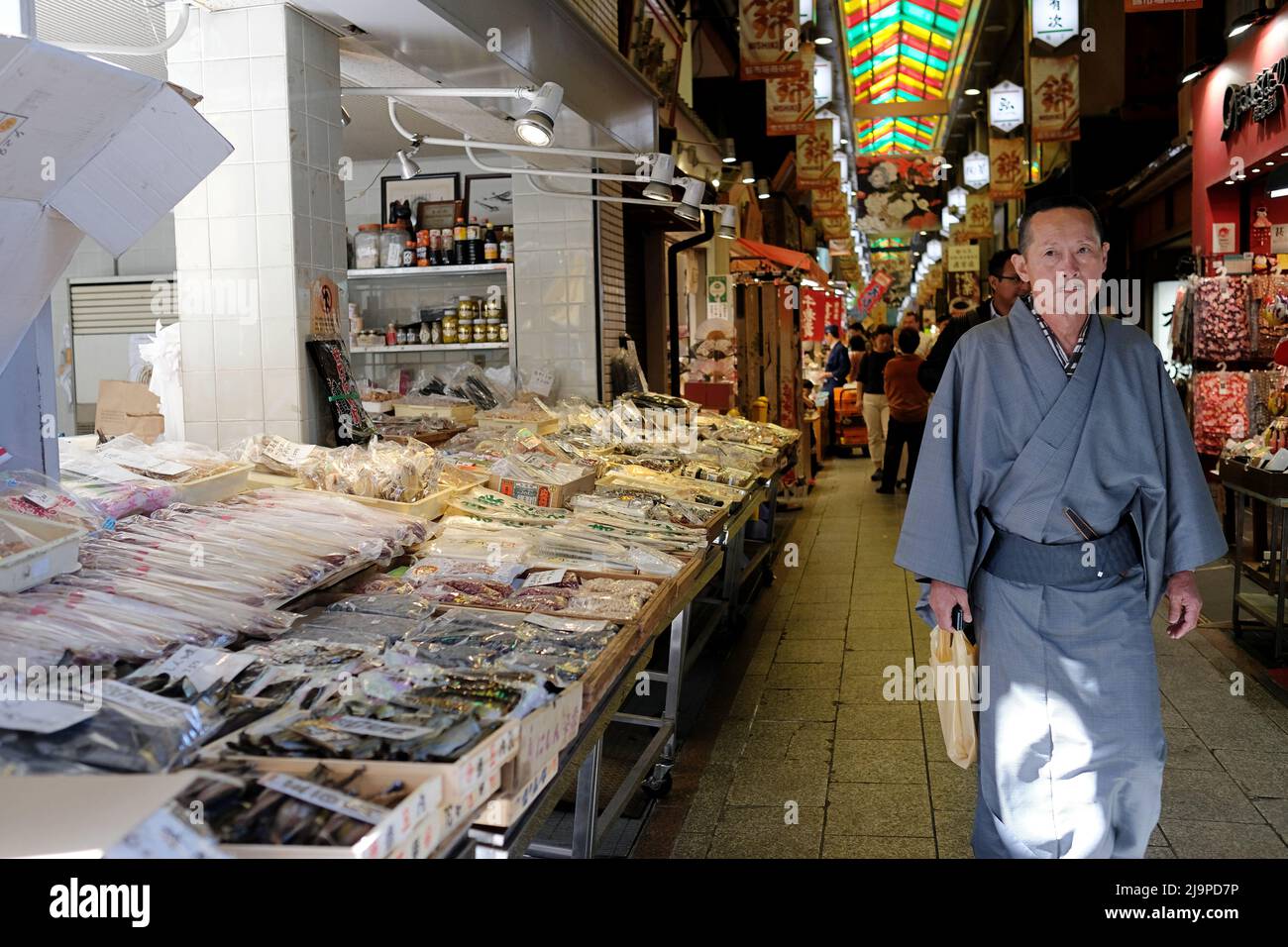 Un uomo giapponese in uno yukata tradizionale cammina davanti a un negozio di prodotti secchi presso i mercati Nishiki a Kyoto, Giappone Foto Stock