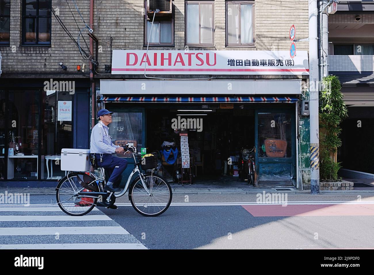 Un uomo giapponese in bicicletta passa accanto a una serie di negozi a Kawaramachi - un quartiere del centro di Kyoto, Giappone. Foto Stock