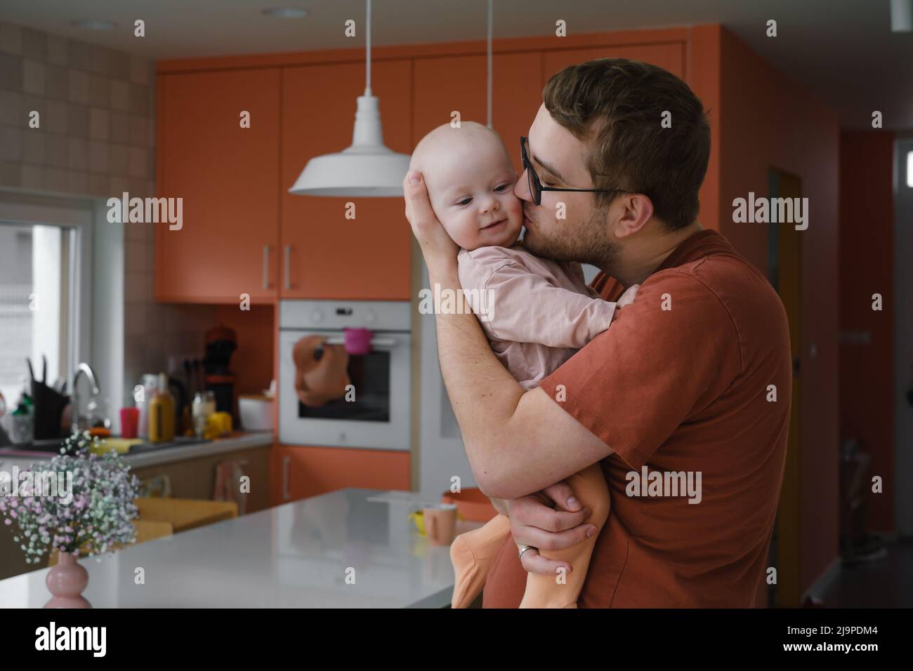 Papà con la bambina nelle sue mani che coccola in cucina a casa, prendendosi cura del bambino. Padre con bambino piccolo. Paternità e ruolo uguale Foto Stock
