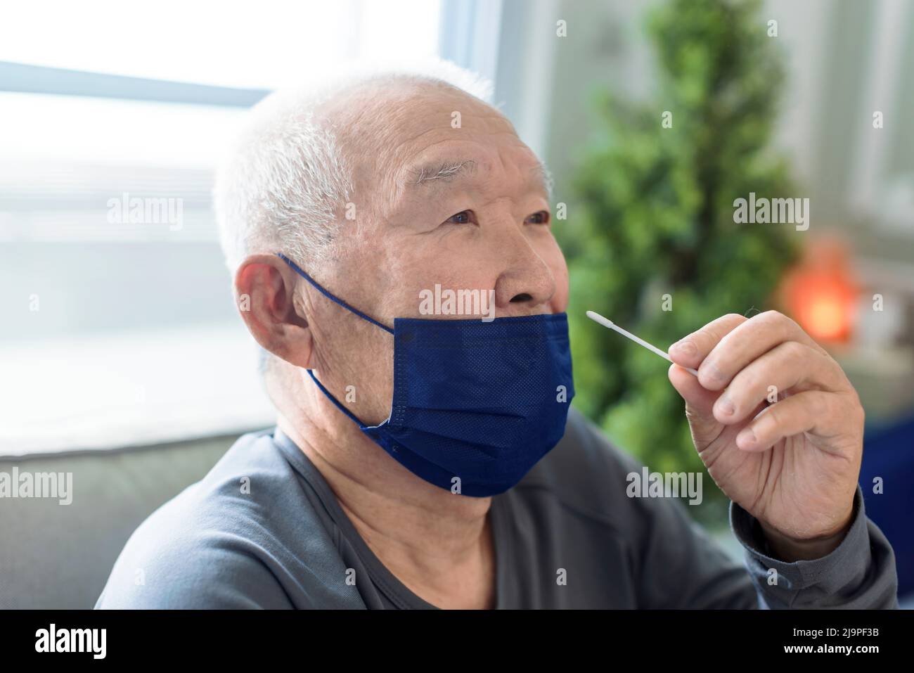 Uomo anziano asiatico che fa auto-test per COVID-19 a casa con kit antigene. Foto Stock