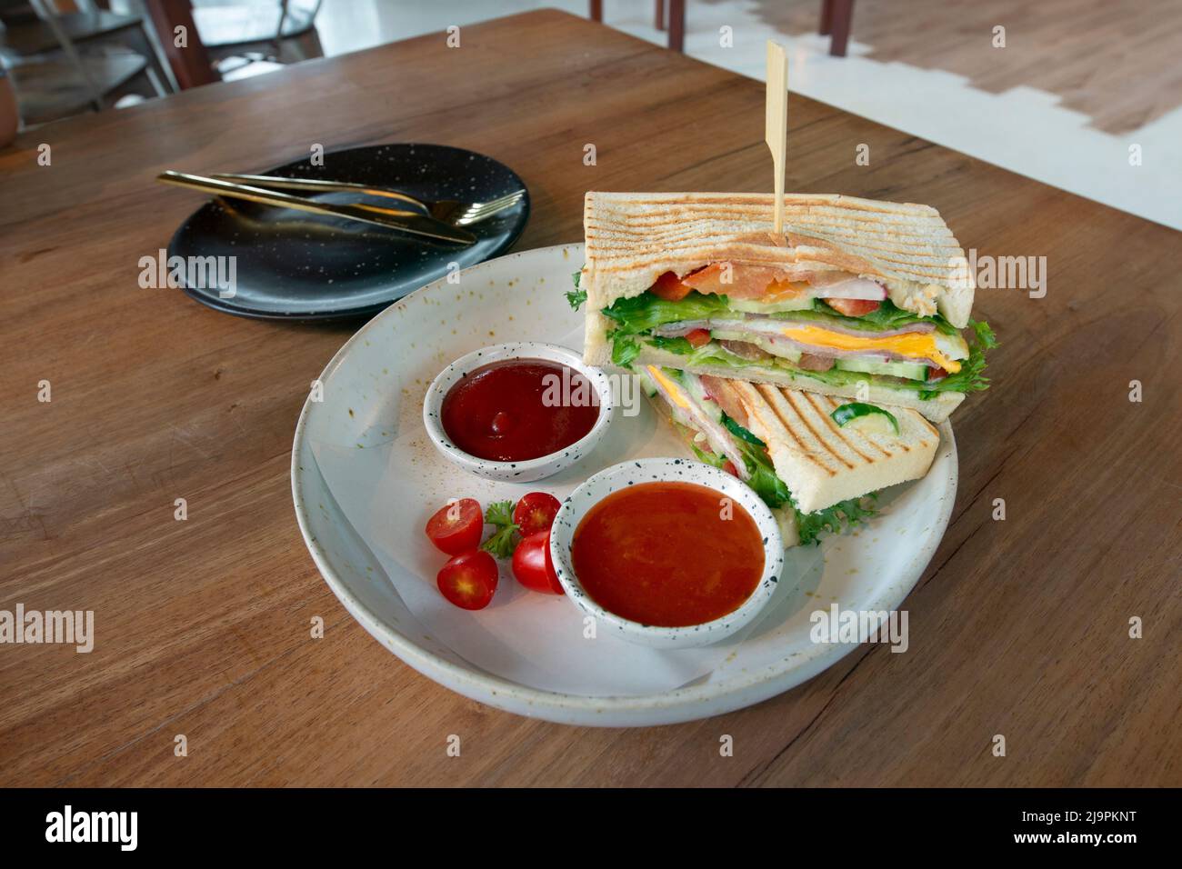 Sandwich posti sul tavolo da pranzo, con ingredienti di prosciutto, uova e fritti freschi, aspetto appetitoso. Panini serviti con ketchup su dini Foto Stock