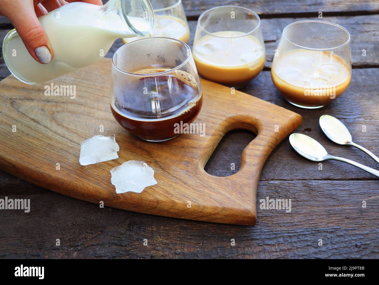 Le donne versano a mano la salsa di latte ghiacciata in un bicchiere di caffè. Rinfrescante drink estivo Foto Stock