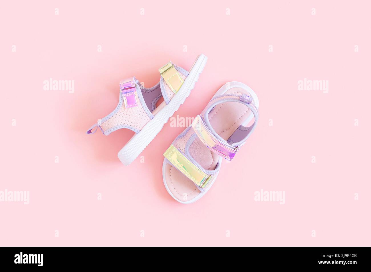 Eleganti sandali olografici per bambini su sfondo rosa. Scarpe estive alla moda lucenti. Disposizione piatta, vista dall'alto. Foto Stock