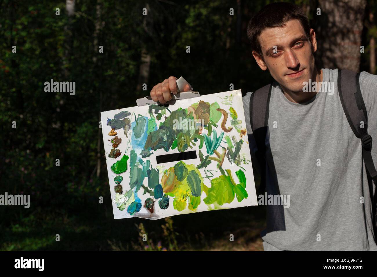 Un ragazzo con una tavolozza di colori. Un artista nella foresta con la sua creazione. Un giovane interessante. Un uomo con un aspetto europeo all'inizio della primavera. Uomo Foto Stock