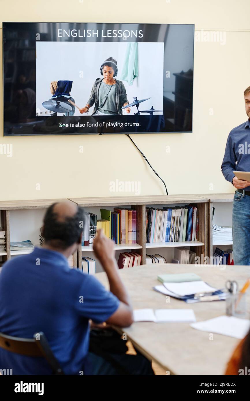Studente nero maturo irriconoscibile che frequenta le lezioni di lingua inglese seduti al tavolo guardando la presentazione sullo schermo della TV Foto Stock