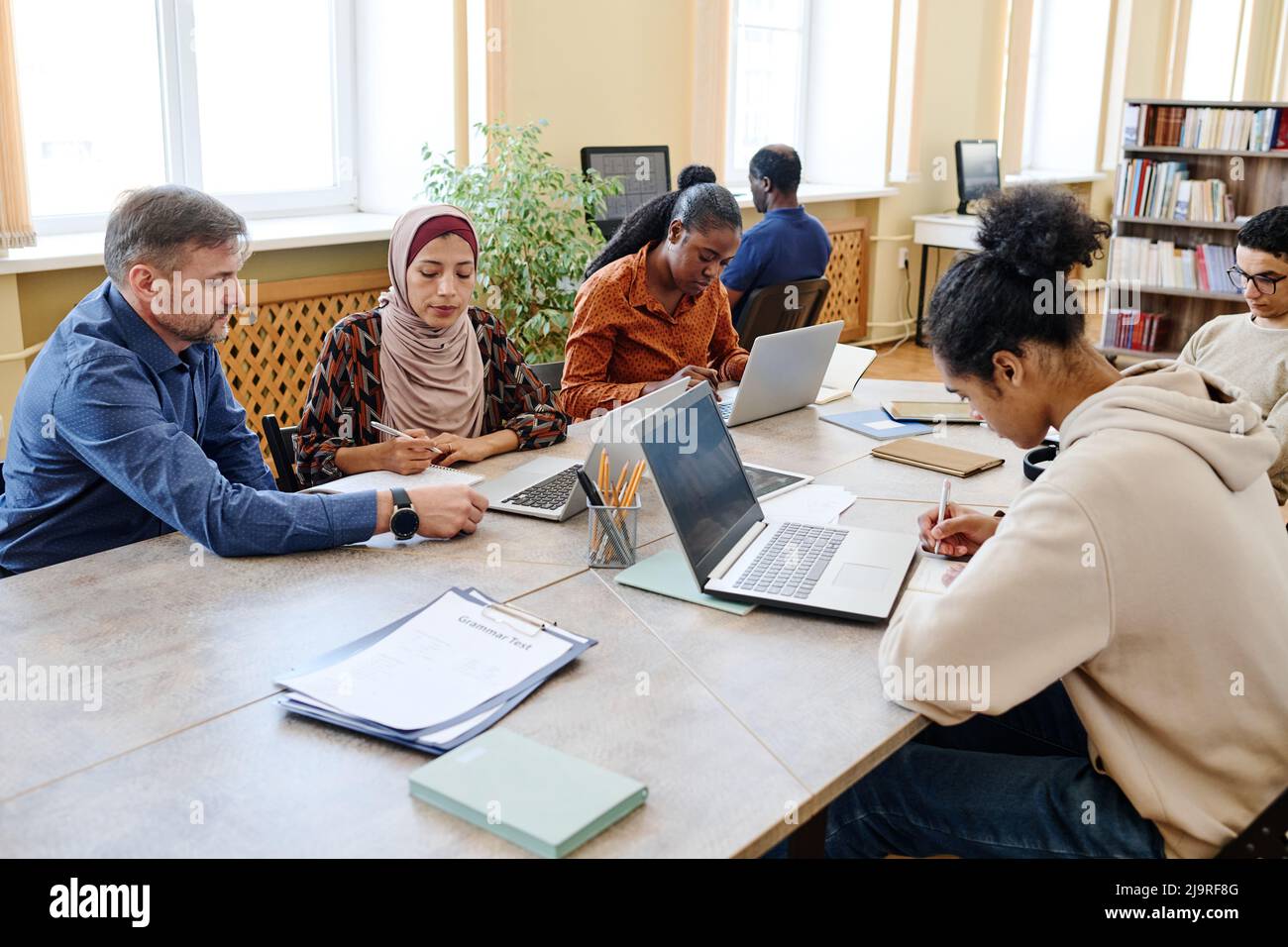 Gruppo di persone multietniche che hanno classi di integrazione e di lingua utilizzando i laptop per svolgere attività di scrittura Foto Stock