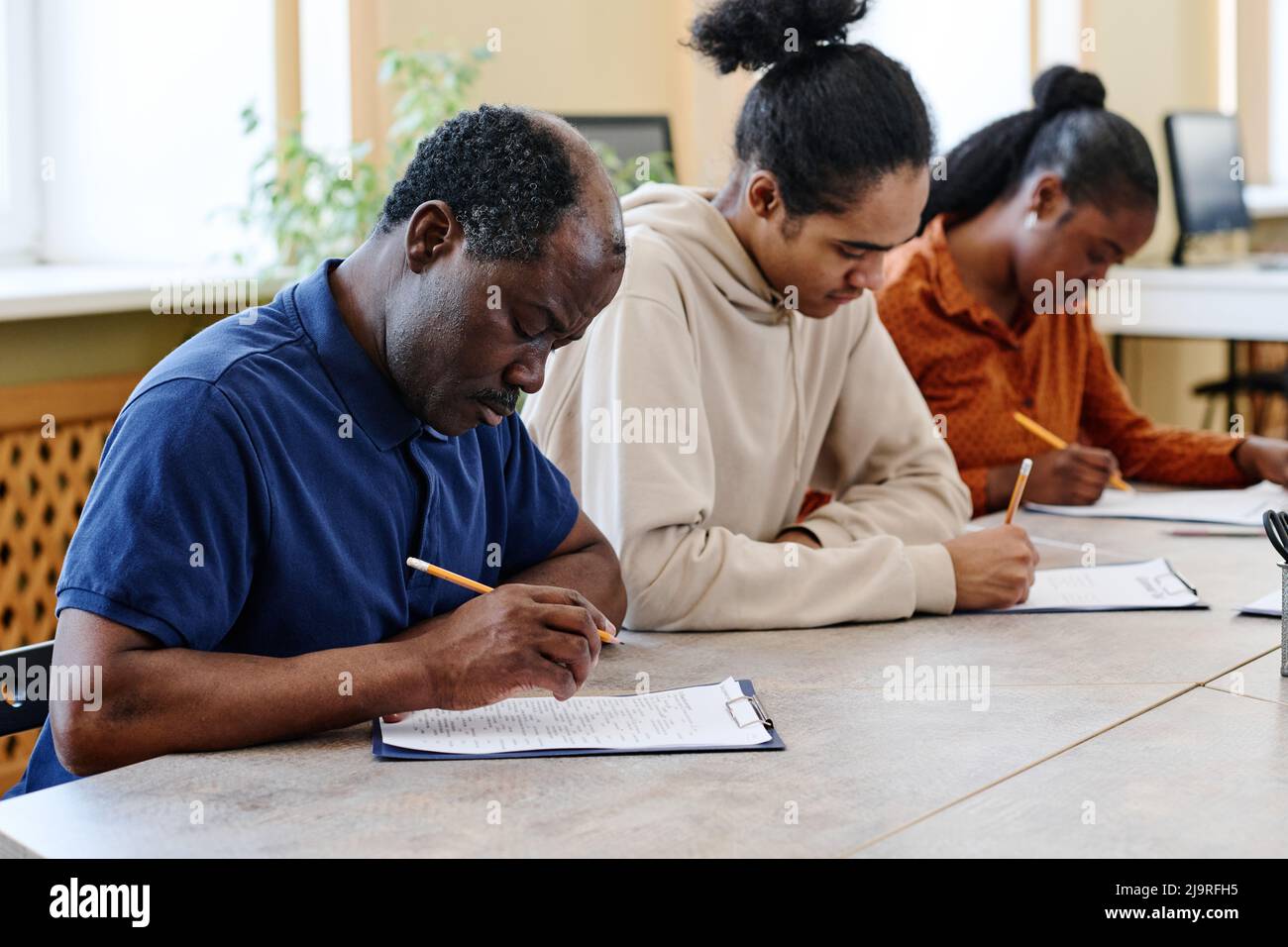 Gruppo di tre persone nere che imparano l'inglese a scuola per gli immigrati seduti a tavola facendo test grammaticali Foto Stock