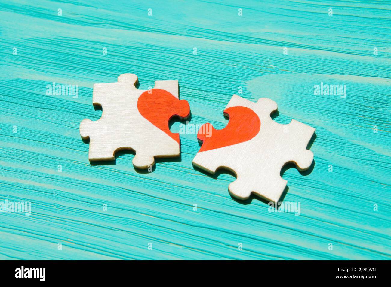 Pezzi di puzzle separati a forma di cuore su sfondo di legno blu. Concetto di relazioni interrotte. Foto Stock