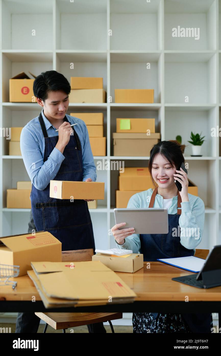 Le coppie asiatiche che fanno le PMI trasportano i loro prodotti in linea ai clienti che ordinano i prodotti via il Internet, aiutanti vendere felicemente: Lavoro dalla sede Foto Stock