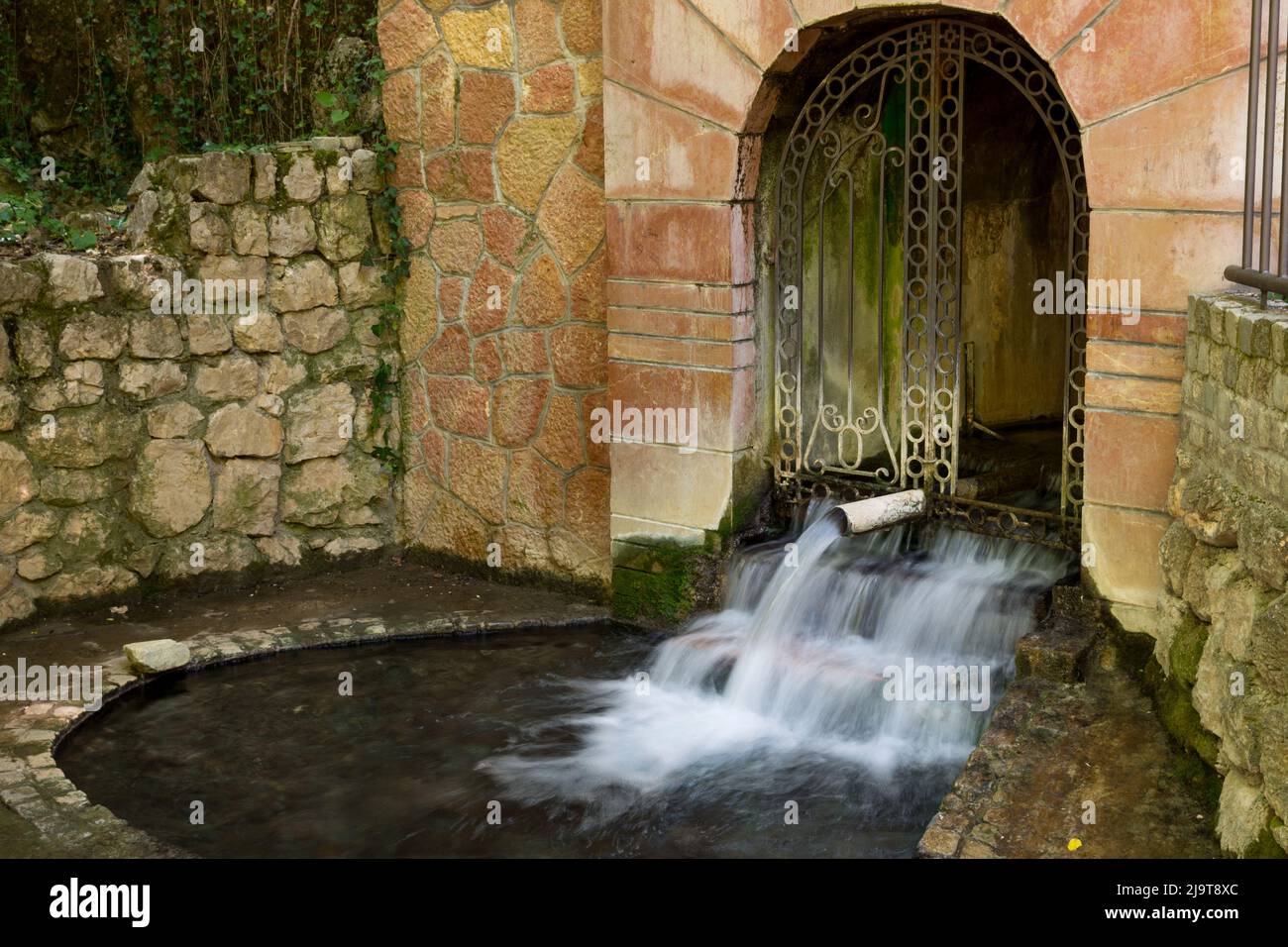 Fonte d'acqua con acqua calda e curativa a NISKA Banja, Serbia, il giorno primaverile. Sorgenti d'acqua dal tunnel nella foresta. Lunga esposizione di acqua Foto Stock