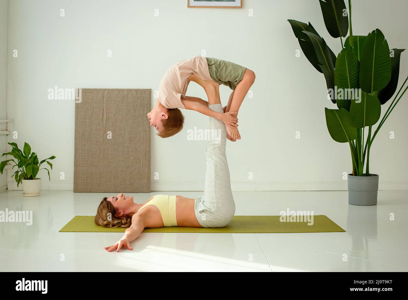 Una donna, che fa yoga con un bambino, si trova su un tappeto sportivo, sollevando le gambe, facendo esercizi di sostegno. Foto Stock
