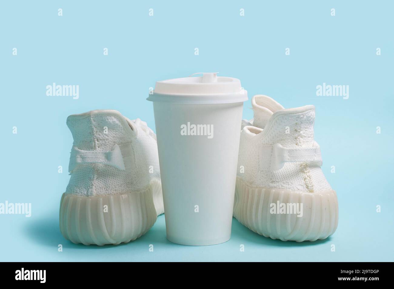 Due sneaker bianche e una tazza di carta bianca con caffè Foto Stock