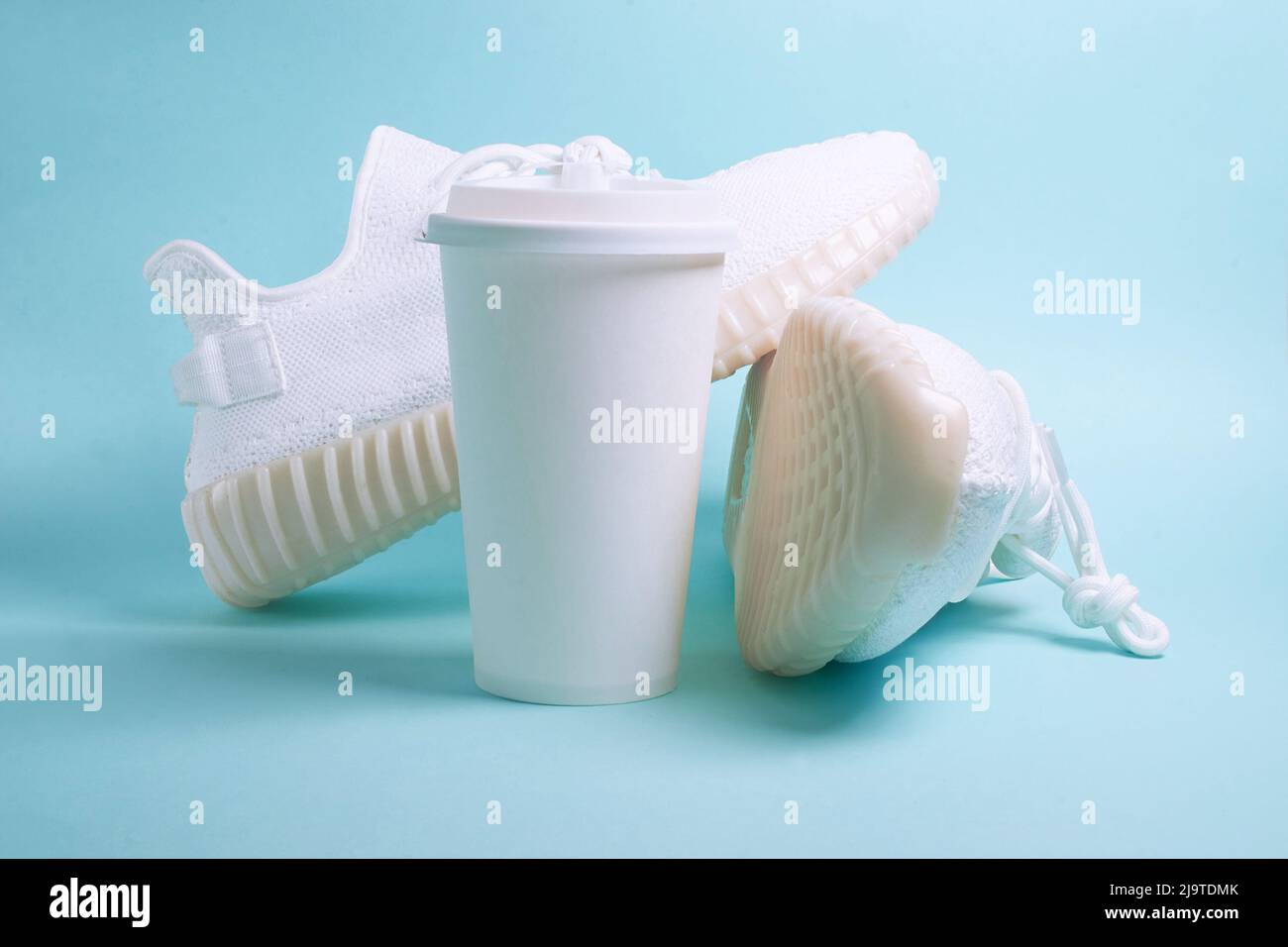 Sneaker bianche e una tazza di carta bianca con caffè Foto Stock