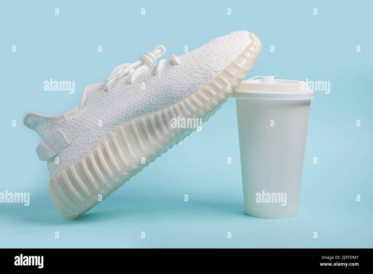 Sneaker bianche e una tazza di carta bianca con caffè Foto Stock