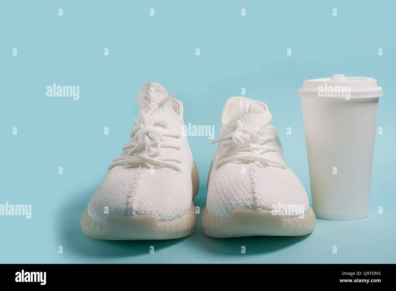 Caffè da gustare. Sneaker bianche e una tazza di carta bianca con caffè Foto Stock