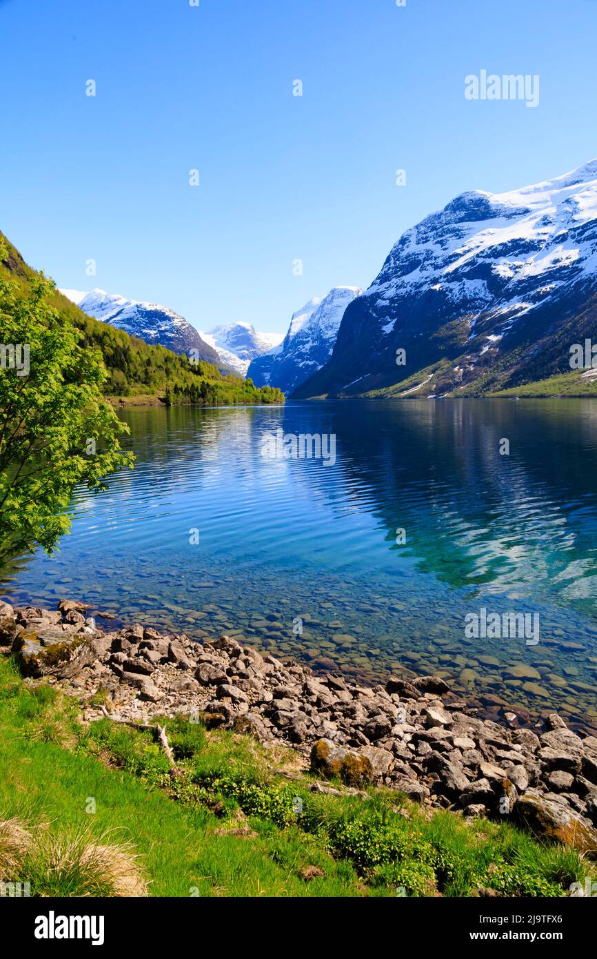 Acqua cristallina e blu sul lago Lovatnet con montagne innevate. Norvegia Foto Stock