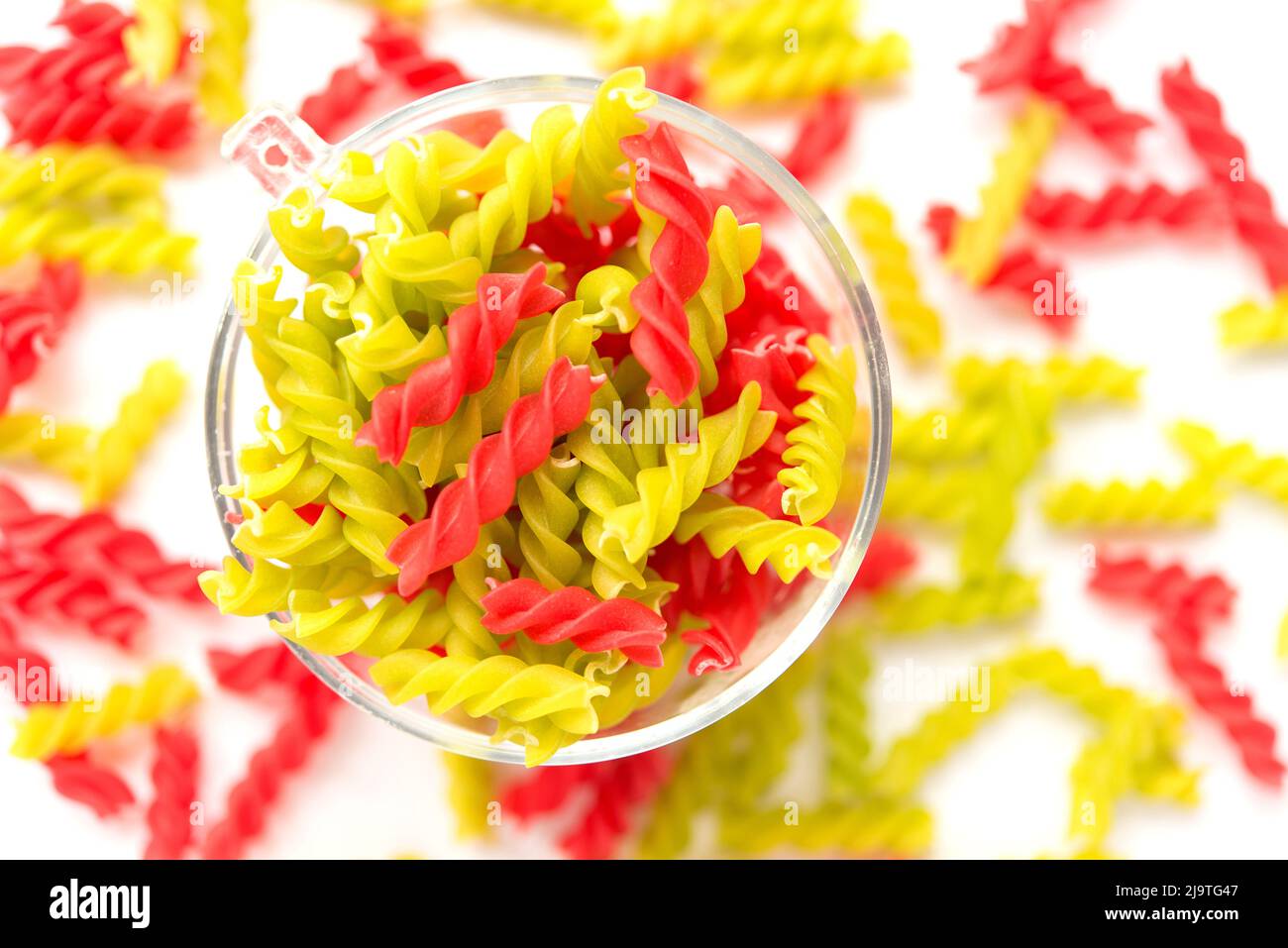 Primo piano sfondo di Fusille e Rotini in una ciotola di vetro su bianco. Pasta colorata Foto Stock