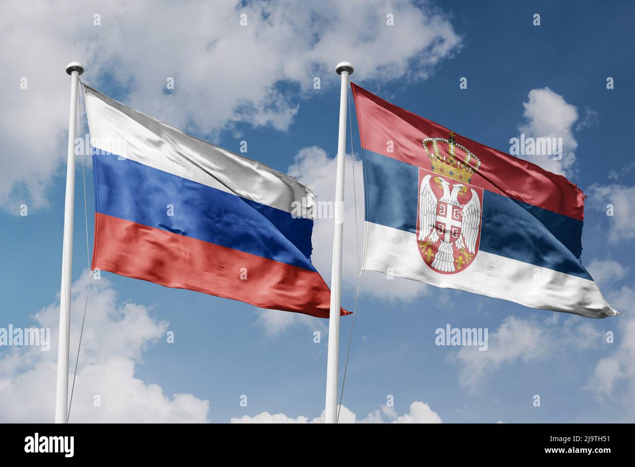 Russia e Serbia due bandiere su flagpoli e cielo blu nuvoloso sfondo Foto Stock