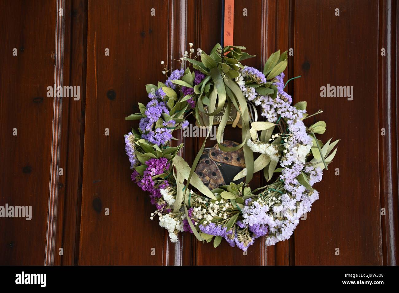 Tradizionale corona di maggio con fiori di amaranto secchi, foglie di  alloro e nastri di raso verde su una porta di legno marrone Foto stock -  Alamy