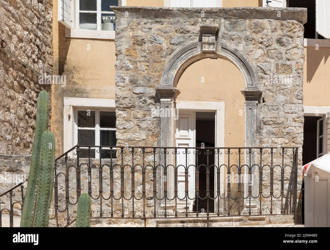 Antico arco in pietra di fronte a una casa color crema nella città di Budvar Montenegro Foto Stock