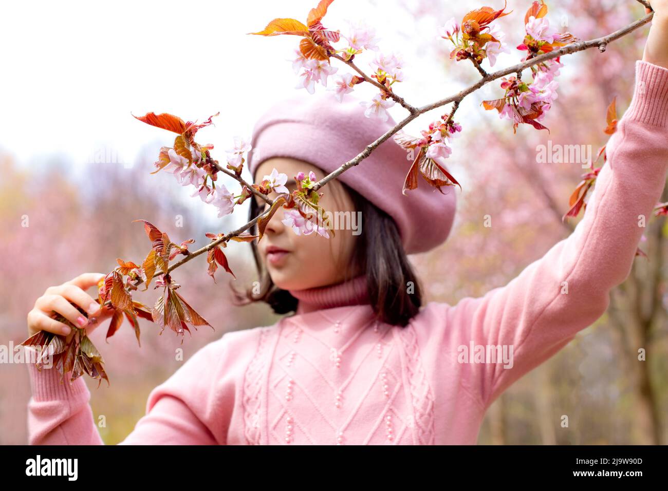 Una bambina in un ponticello rosa tiene un ramo di fiori di ciliegia, nel parco durante il giorno Foto Stock